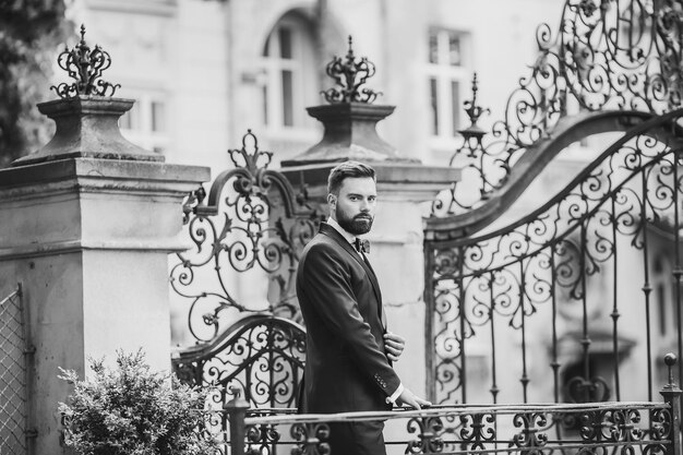 Retrato de un apuesto joven chino con traje azul claro y camiseta blanca caminando y mirando hacia otro lado con el fondo de los edificios de la ciudad moderna en la vista lateral del día soleado de un hombre de negocios confiado