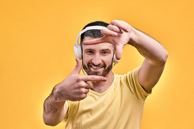 Retrato de un apuesto joven con elegantes auriculares blancos que muestra un marco con los dedos