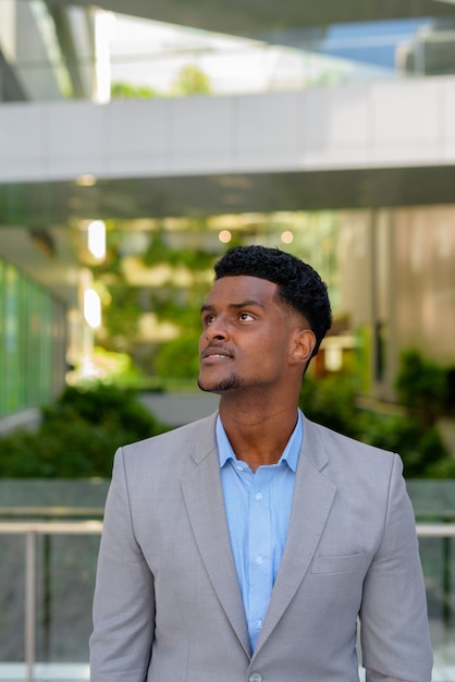 Retrato de apuesto joven empresario africano pensando al aire libre