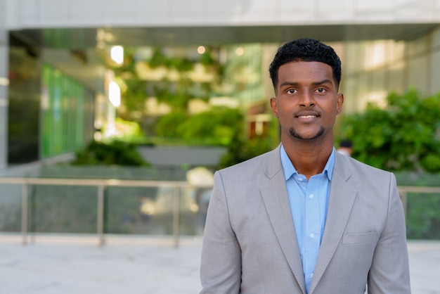 Retrato de apuesto joven empresario africano sonriendo al aire libre