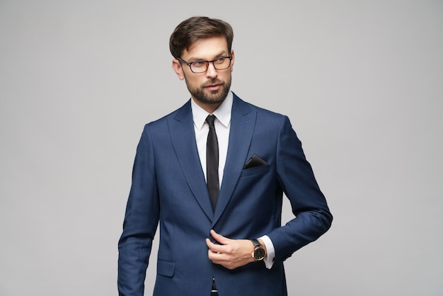 Retrato de un apuesto joven empresario elegante con gafas sobre pared gris