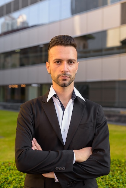 Retrato de apuesto joven empresario italiano al aire libre en la ciudad vistiendo traje