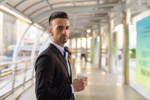 Retrato de apuesto joven empresario italiano al aire libre en la ciudad vistiendo traje