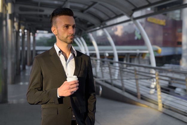 Retrato de apuesto joven empresario italiano al aire libre en la ciudad vistiendo traje