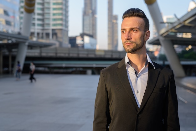 Retrato de apuesto joven empresario italiano al aire libre en la ciudad vistiendo traje