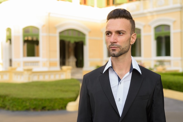 Retrato de apuesto joven empresario italiano al aire libre en la ciudad vistiendo traje