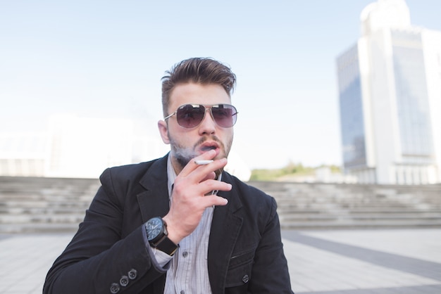 Retrato de un apuesto joven empresario sonriendo un cigarrillo en una ciudad