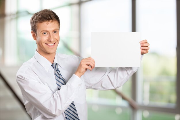 Retrato de apuesto joven empresario sosteniendo pancartas en blanco y mirando a cámara en la oficina