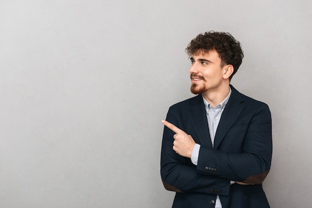 retrato de un apuesto joven hombre de negocios aislado sobre pared gris apuntando.