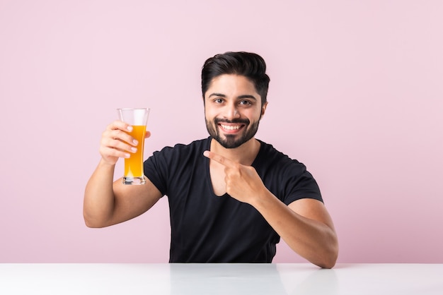 Retrato de un apuesto joven indio bebiendo jugo de naranja en la cocina por la mañana