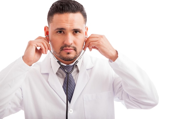 Retrato de un apuesto joven médico latino poniéndose el estetoscopio antes de examinar a un paciente