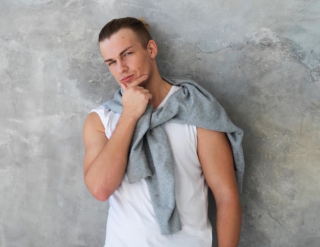 Retrato de un apuesto joven modelo de moda posando sobre una pared gris