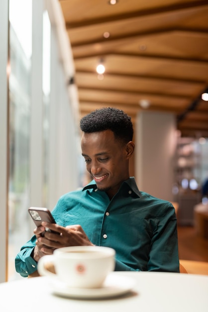 Retrato de un apuesto joven negro en una cafetería usando el teléfono