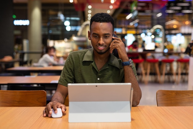 Retrato de un apuesto joven negro que usa una computadora portátil en una cafetería