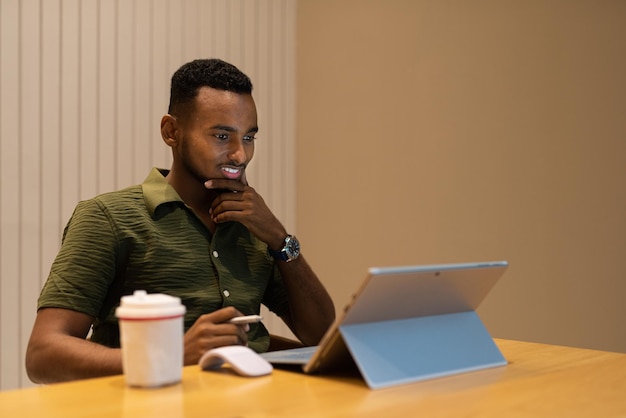 Retrato de un apuesto joven negro que usa una computadora portátil en una cafetería