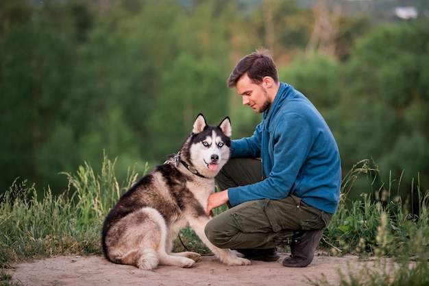 Retrato de un apuesto joven y su mascota perro Husky siberiano en la naturaleza por la noche al atardecer