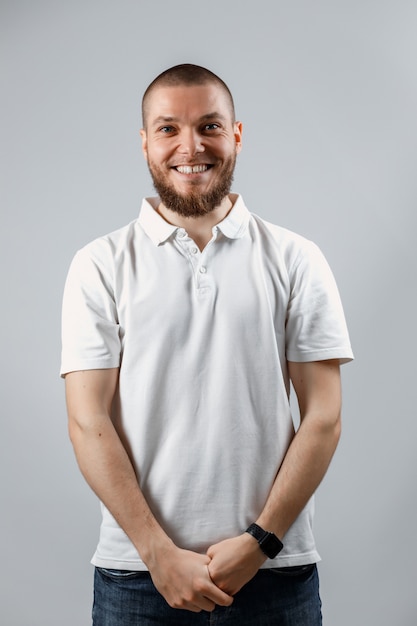 Retrato de un apuesto joven tímido en una camiseta blanca sobre gris