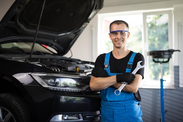 Retrato de un apuesto mecánico automotriz con uniforme azul parado en el servicio de vehículos de garaje