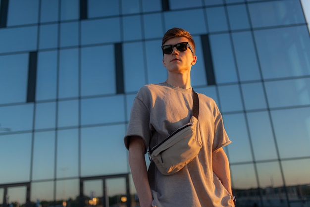 Foto retrato de un apuesto turista hipster con gafas de sol con un bolso a mano cerca del edificio en el centro tranquilo momento relajante concepto de vacaciones de verano