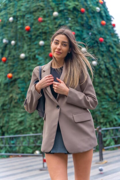 Retrato por el árbol de navidad en la ciudad joven mujer sonriente en una gabardina