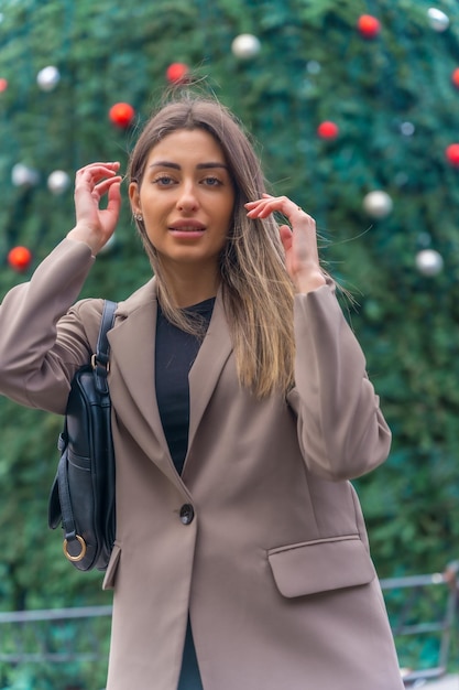 Retrato por el árbol de navidad en la ciudad mujer joven en una gabardina mirando a la cámara