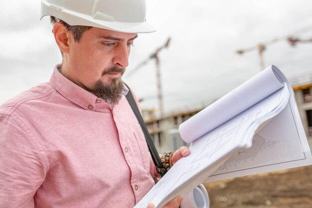 Retrato del arquitecto en el trabajo con casco en un sitio de construcción, lee el plan.