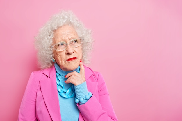 Retrato de arrugada dama senior de cabello gris pensativa concentrada a un lado recuerda su juventud vestida con ropa de moda tiene vestidos de maquillaje brillante para ocasiones especiales