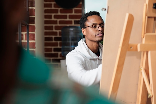 Retrato de un artista afroamericano dibujando un jarrón sobre lienzo durante la clase de arte aprendiendo la técnica de ilustración usando un lápiz gráfico. Estudiante de pintor asistiendo al taller de creatividad.