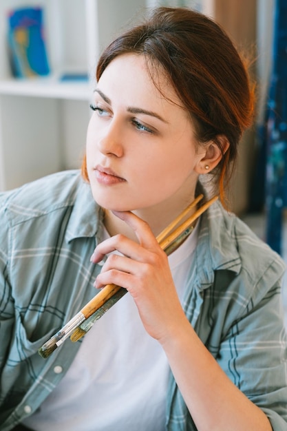 Retrato de artista Estilo de vida creativo Imaginación talento Inspirado mujer pensativa pacífica con pinceles manojo soñando despierto en estudio de arte ligero