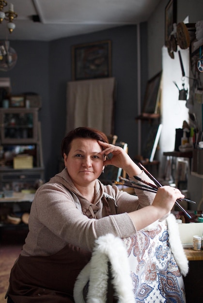 Retrato de una artista femenina en un estudio de arte sentada en una silla con pinceles en la mano