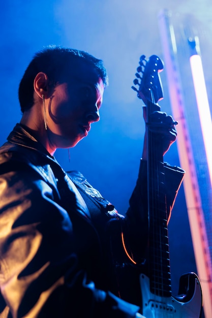 Retrato de un artista rockstar tocando guitarra eléctrica ajustando el sonido antes de un concierto de rock, compositor trabajando en una canción de heavy metal. Mujer superestrella con estilo rebelde preparando álbum punk en estudio