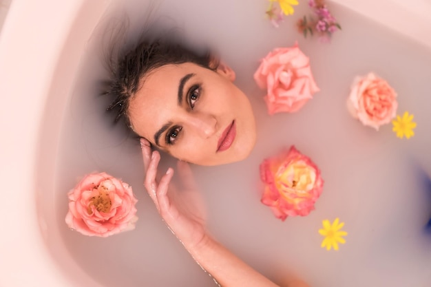 Retrato artístico desde arriba de una mujer en un baño en leche llena de flores