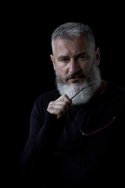 Foto retrato artístico de un brutal hombre de pelo gris con barba y gafas sobre un fondo negro, enfoque selectivo