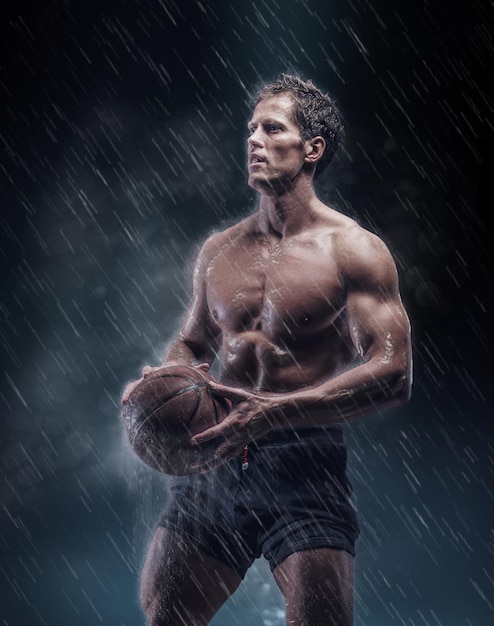 Retrato artístico de jogador de basquete molhado sem camisa sob gotas.