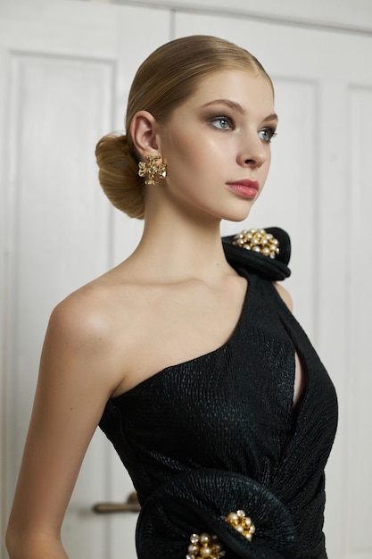 Retrato artístico de un moño de pelo de mujer rubia joven Hermosa mujer en vestido de noche negro Maquillaje de noche perfecto en el retrato de estudio de moda de peinado de cara de mujer elegante hermosa en negro