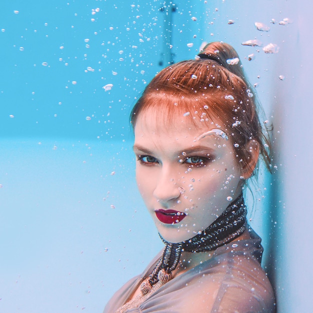 retrato artístico surrealista de una joven vestida de gris y bufanda con cuentas bajo el agua en la piscina