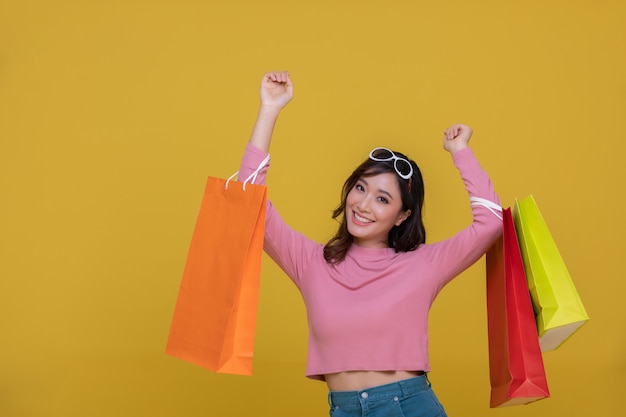 Retrato de Asia hermosa joven feliz sonriendo alegre y sosteniendo bolsas de compras aisladas en amarillo