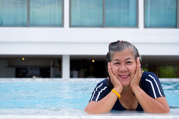 Foto retrato de asia mujer madura de pie en una piscina poniendo su barbilla en la mano y mirando hacia adelante