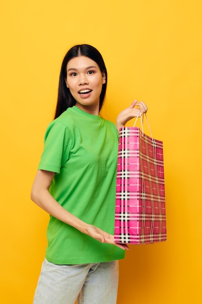 Retrato asiático hermosa mujer joven con bolsa de regalo en manos divertido fondo amarillo inalterado