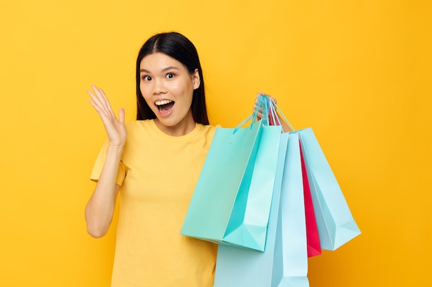 Retrato asiático hermosa mujer joven en una camiseta amarilla con bolsas de compras multicolores modelo de estudio inalterado