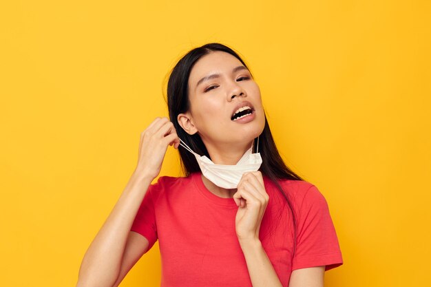 Retrato asiático hermosa mujer joven en camiseta roja máscara médica protección fondo amarillo inalterado