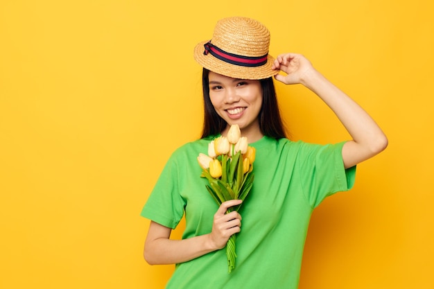 Retrato asiático hermosa mujer joven posando con un ramo de flores en un fondo amarillo sombrero inalterado