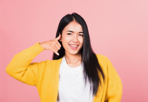 Retrato asiático hermosa mujer joven sonriendo haciendo gesto de teléfono con la mano y los dedos como hablar por teléfono, estudio tiro fondo rosa aislado, gesto de comunicación femenina tailandesa