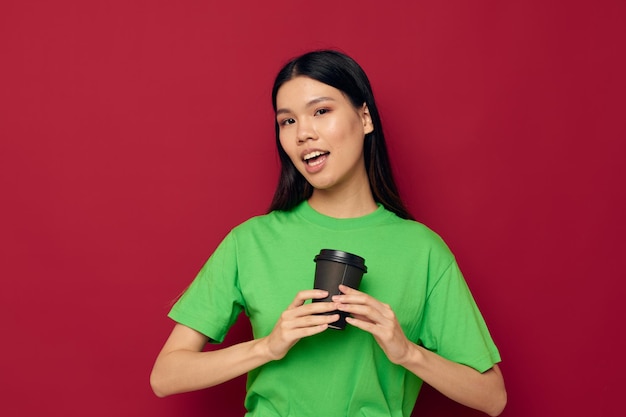 Retrato asiático hermosa mujer joven sonrisa camiseta verde negro vasos desechables moda fondo rojo inalterado