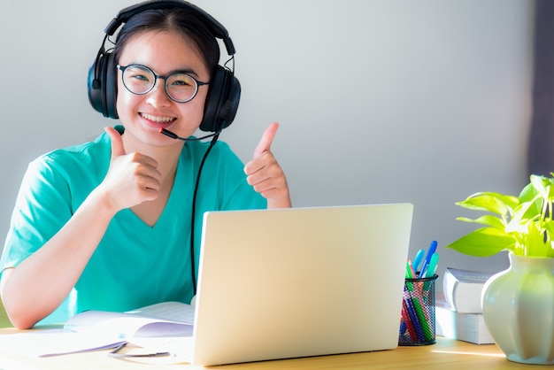 Retrato asiático jovem estudante óculos fones de ouvido estudo feliz sorriso olhando dois polegares para cima aula online faculdade aprendizagem internet educação adolescente trabalho distância em um laptop de casa