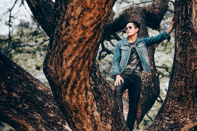 Retrato asiático jóvenes con gafas de sol y jeans camisas de pie en el árbol