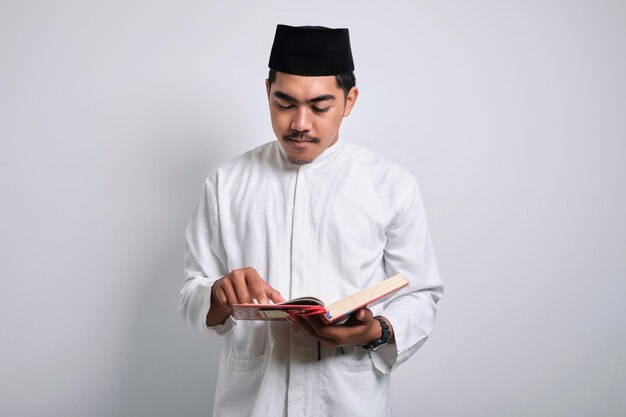 Foto retrato asiático musulmán hombre de pie y leyendo el corán aislado sobre fondo blanco.