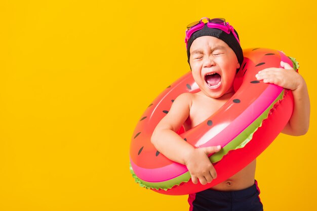 Retrato asiático niño pequeño niño usar gafas y traje de baño sostener anillo inflable de sandía