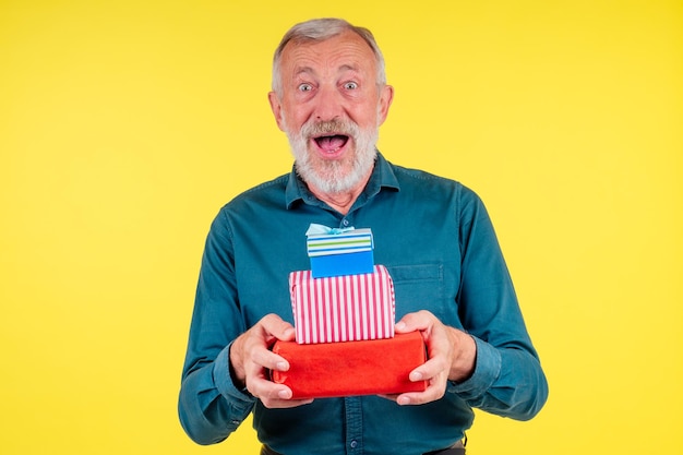 Retrato asombrado anciano caucásico sosteniendo dos boxex de regalos en estudio fondo amarillo.