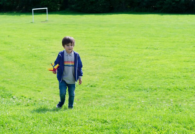 Retrato ativo menino brincando com o avião de brinquedo contra a natureza verde